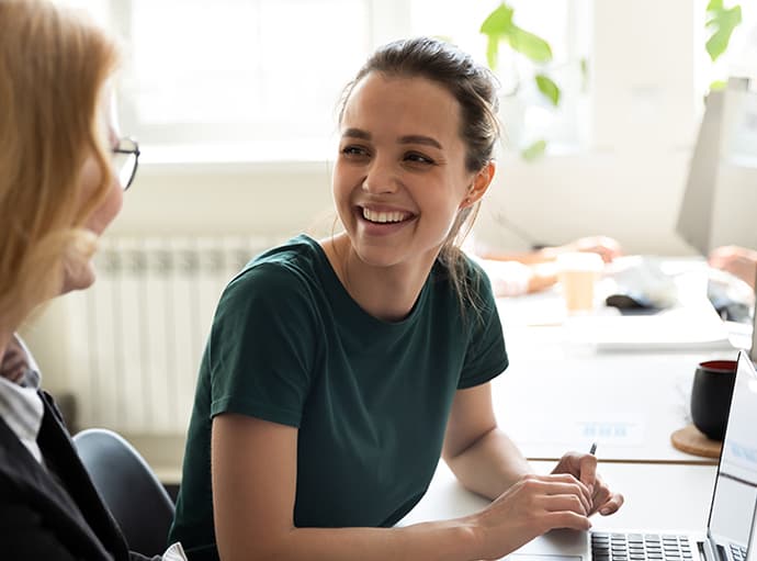 A young woman is smiling at another woman in an office environment